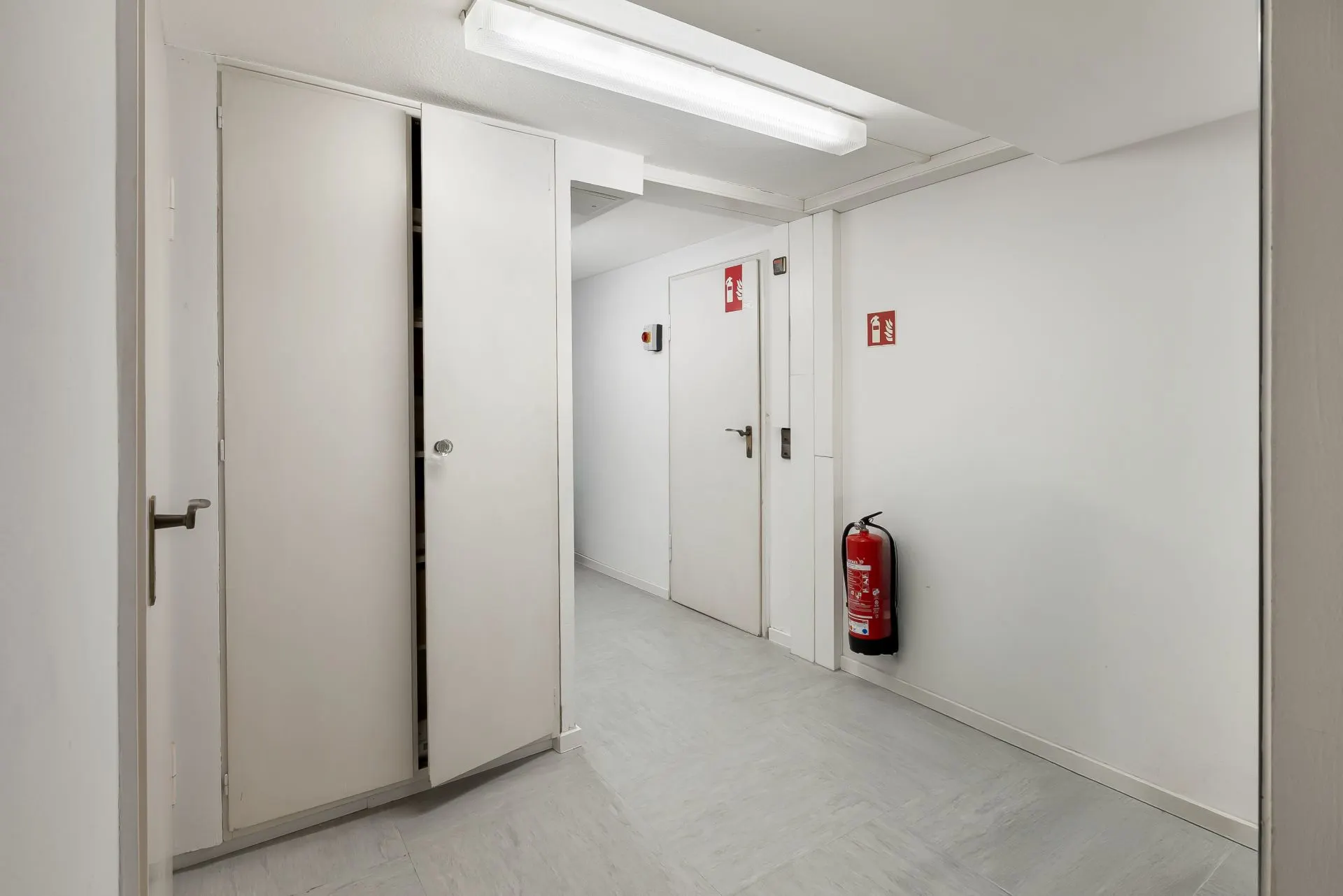 Heller Flur mit weißen Türen, Wandschrank und Feuerlöscher an der Wand.