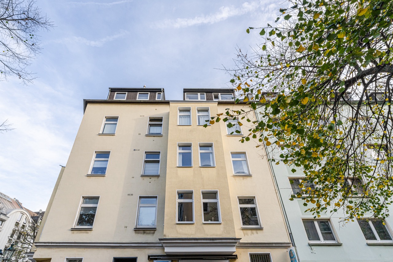 Mehrstöckiges Wohnhaus mit gelber Fassade und mehreren Fenstern, Baum rechts im Vordergrund.