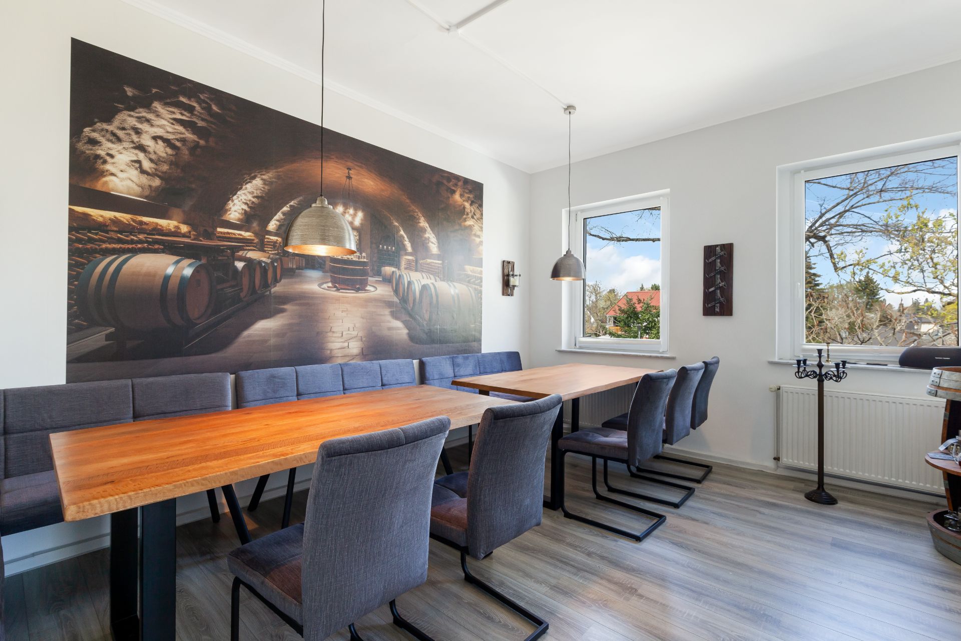 Esszimmer mit langem Holztisch, gepolsterten Stühlen und Wandbild eines Weinkellers.