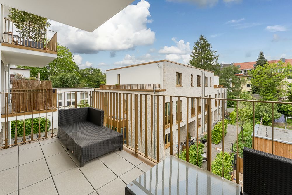 Modern eingerichteter Balkon mit Sitzbank und Blick auf Nachbarhäuser und grüne Bäume.