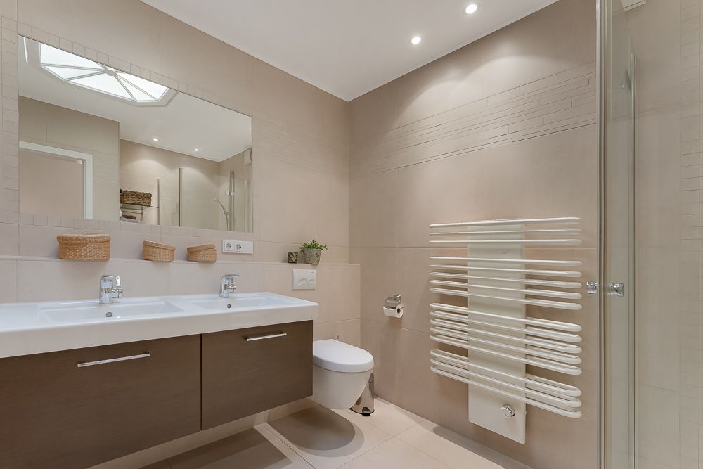 Modernes Badezimmer mit Doppelwaschbecken, großem Spiegel, WC und Handtuchheizkörper.