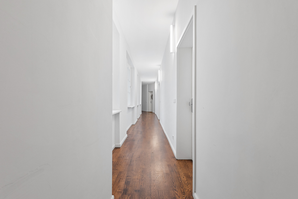 Langer, heller Flur mit weißen Wänden und Holzboden in einem Wohngebäude.