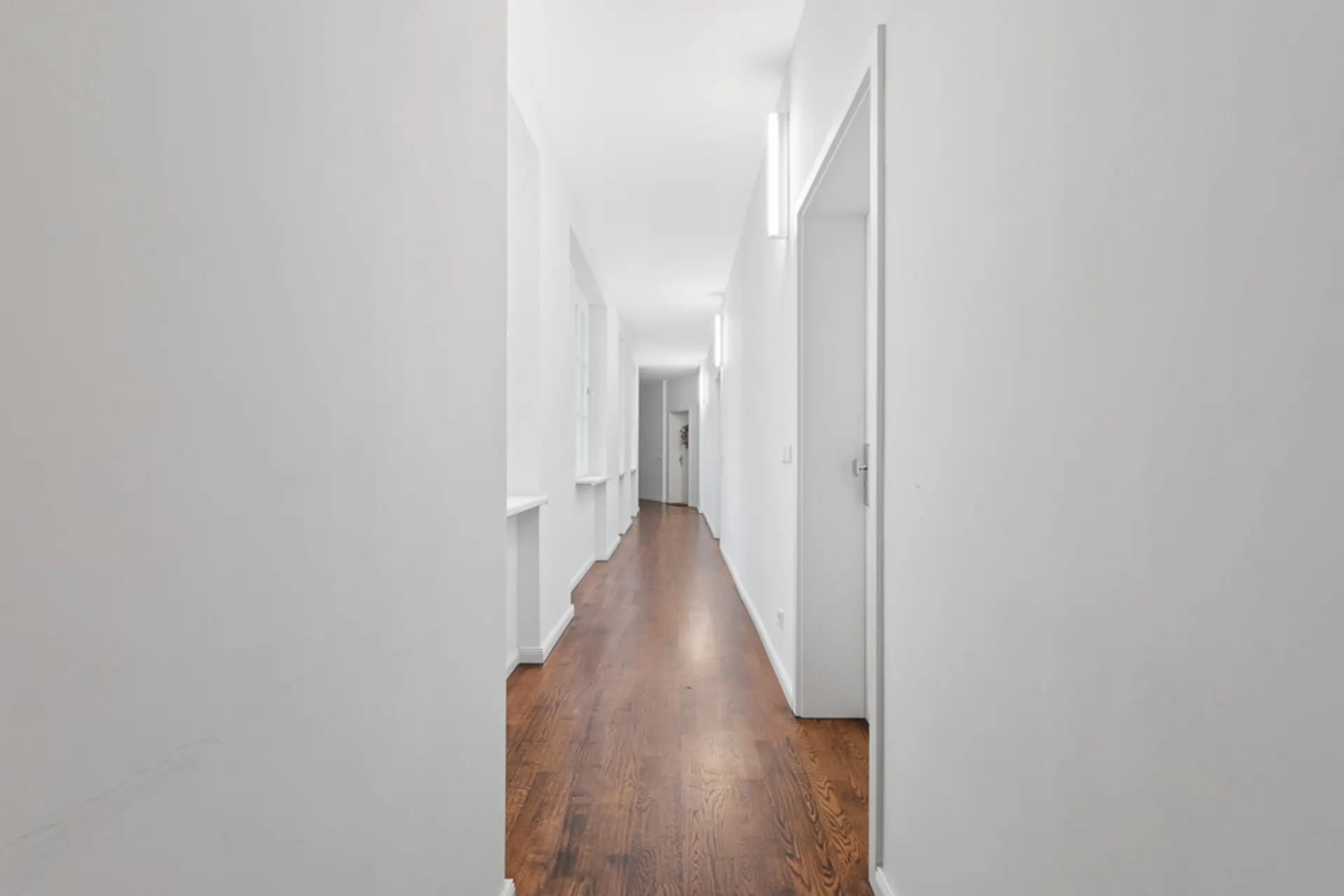 Langer, heller Flur mit weißen Wänden und Holzboden in einem Wohngebäude.
