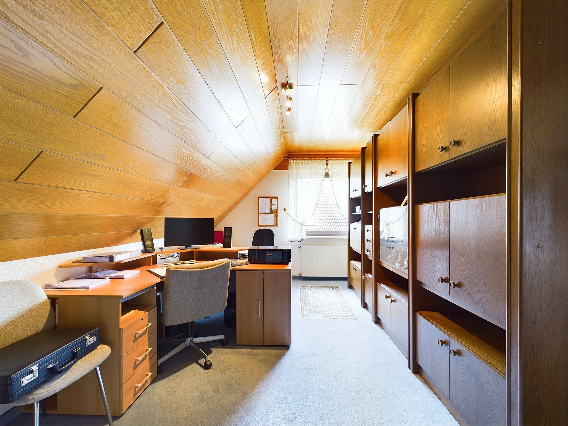 Helles Arbeitszimmer mit Schräge, Schreibtisch, zwei Stühlen und Regalen aus Holz.