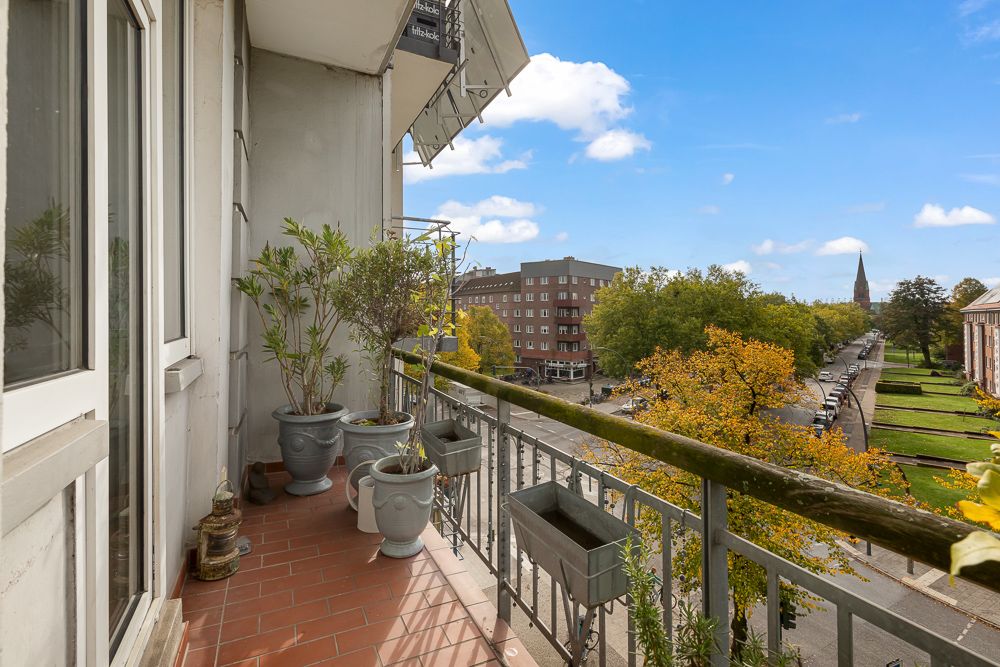 Balkon mit Pflanzkübeln und Blick auf eine Straße mit Bäumen und Gebäuden.