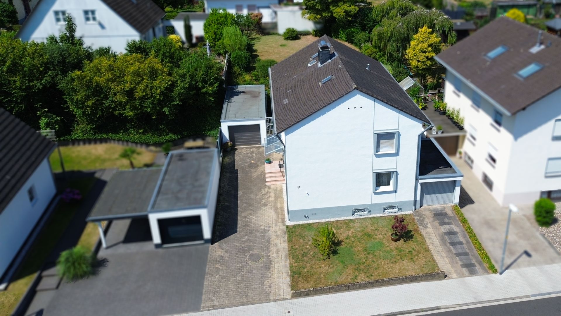 Luftaufnahme eines weißen Wohnhauses mit Garage, Einfahrt und kleinem Vorgarten.