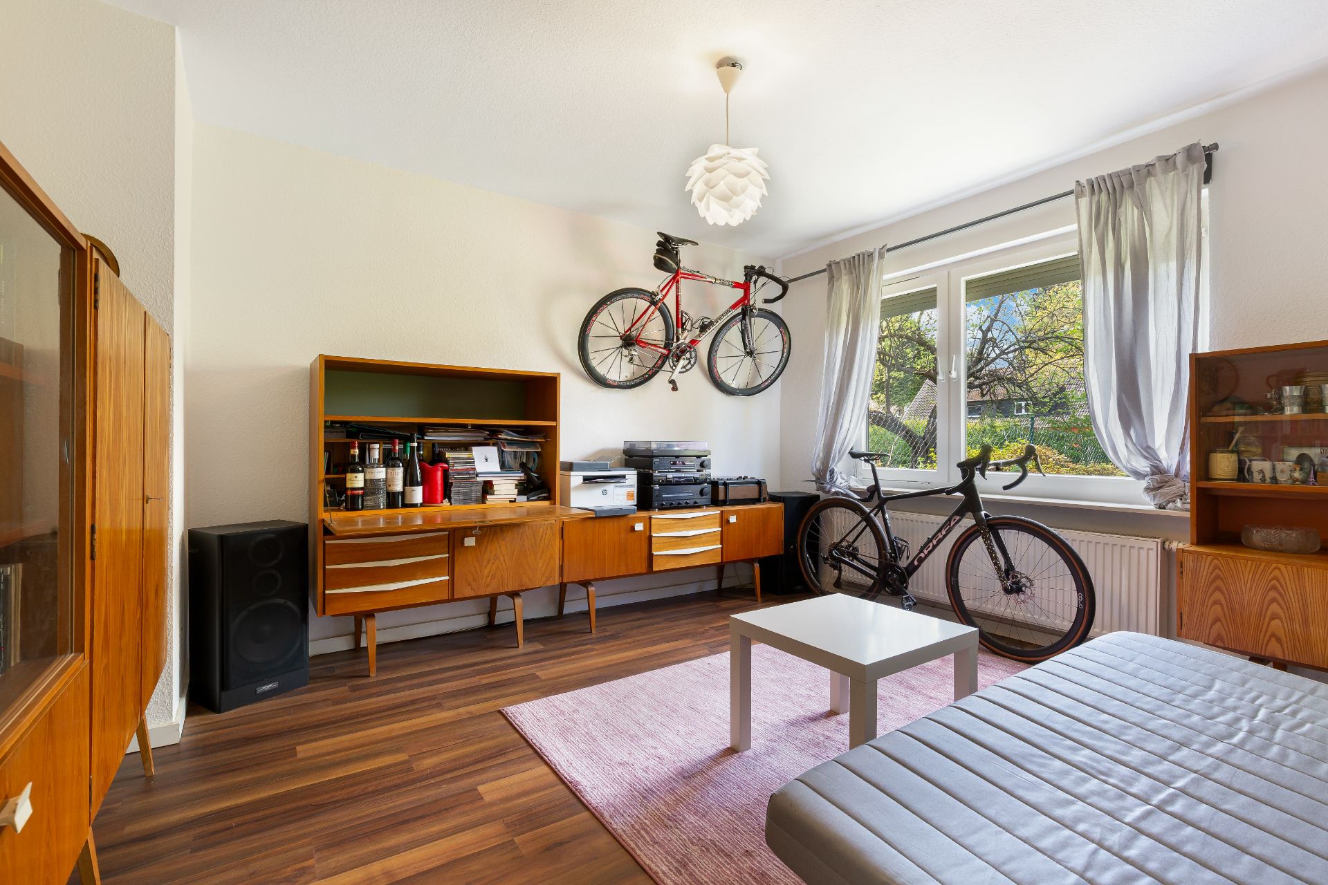Helles Wohnzimmer mit Holzmöbeln, zwei Fahrrädern, einem Sofa und einem Fenster mit Blick nach draußen.