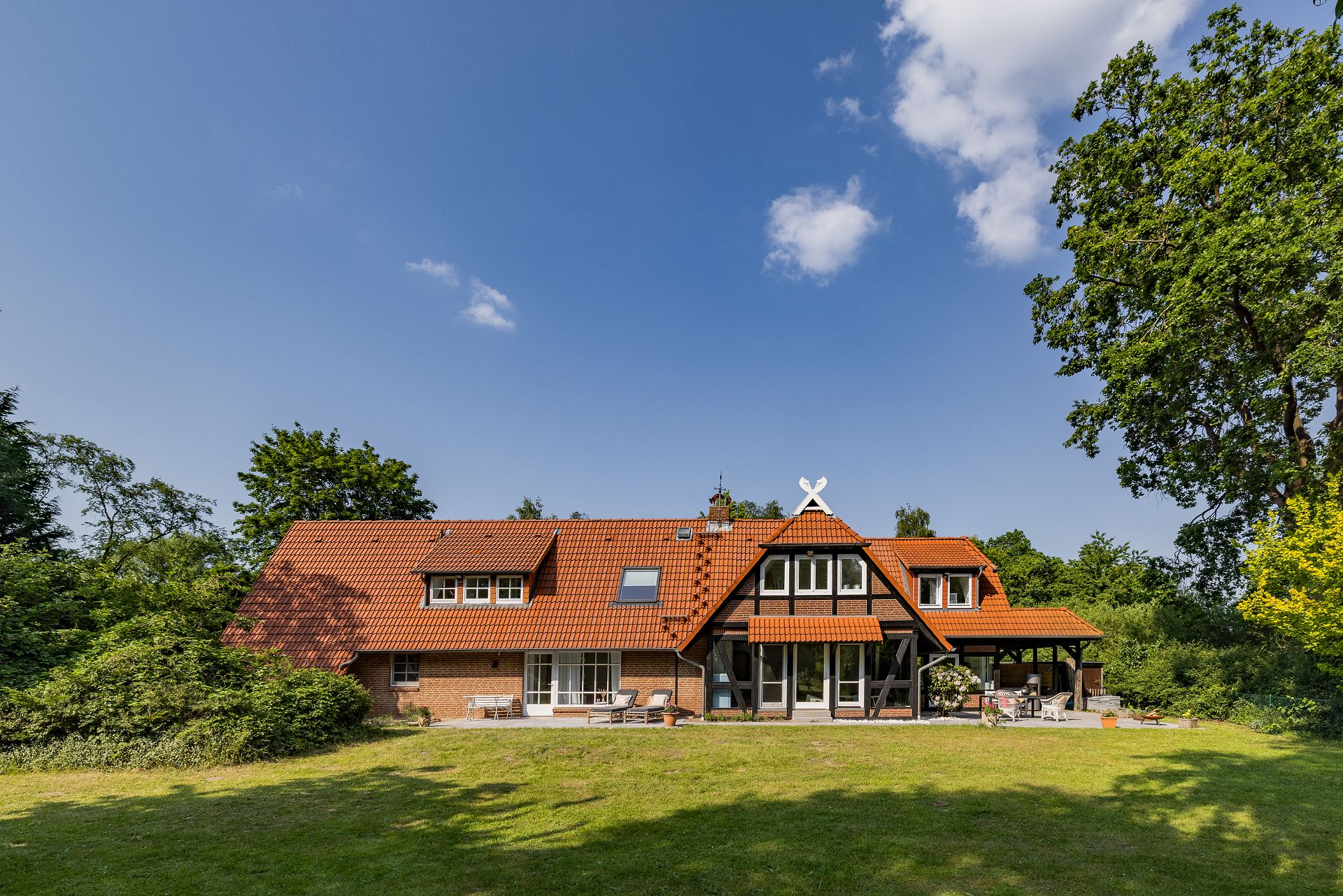 Großes Wohnhaus mit rotem Dach, Terrasse und Garten, umgeben von Bäumen.