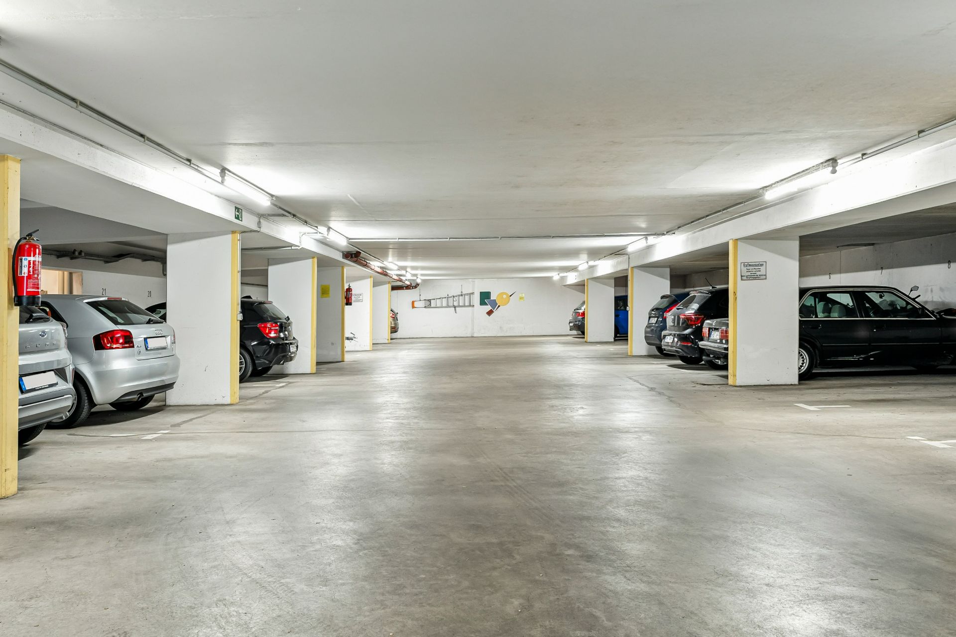 Helle Tiefgarage mit geparkten Autos und bemalter Wand im Hintergrund.