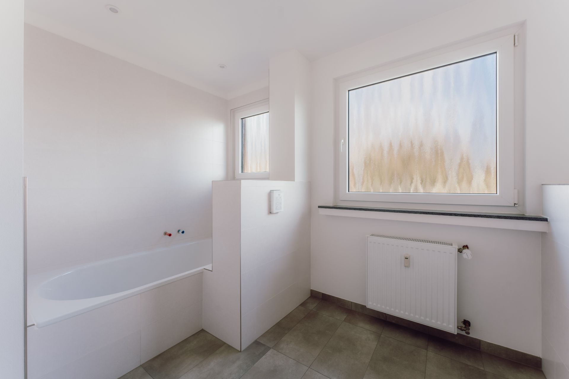 Helles Badezimmer mit Badewanne, großem Fenster und Heizkörper.