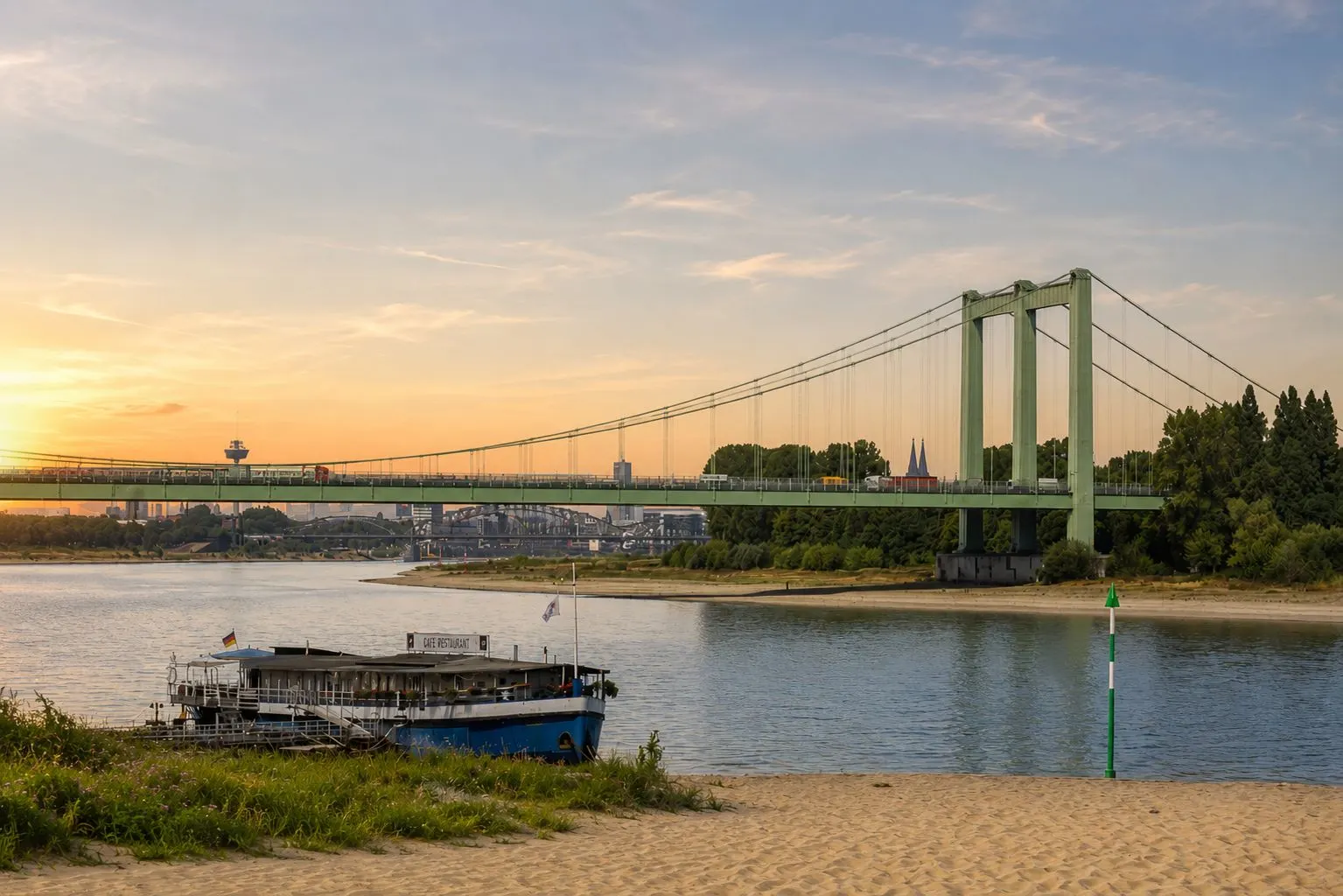 Grüne Hängebrücke über einen Fluss mit Boot im Vordergrund und Bäumen im Hintergrund.