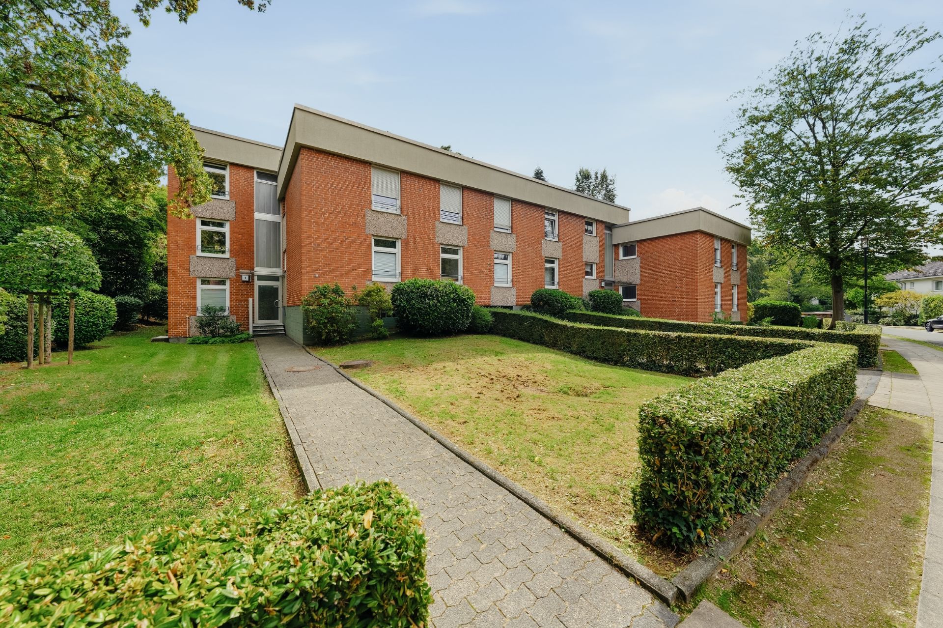 Zweistöckiges Wohnhaus aus rotem Backstein mit gepflegtem Vorgarten und Hecken.