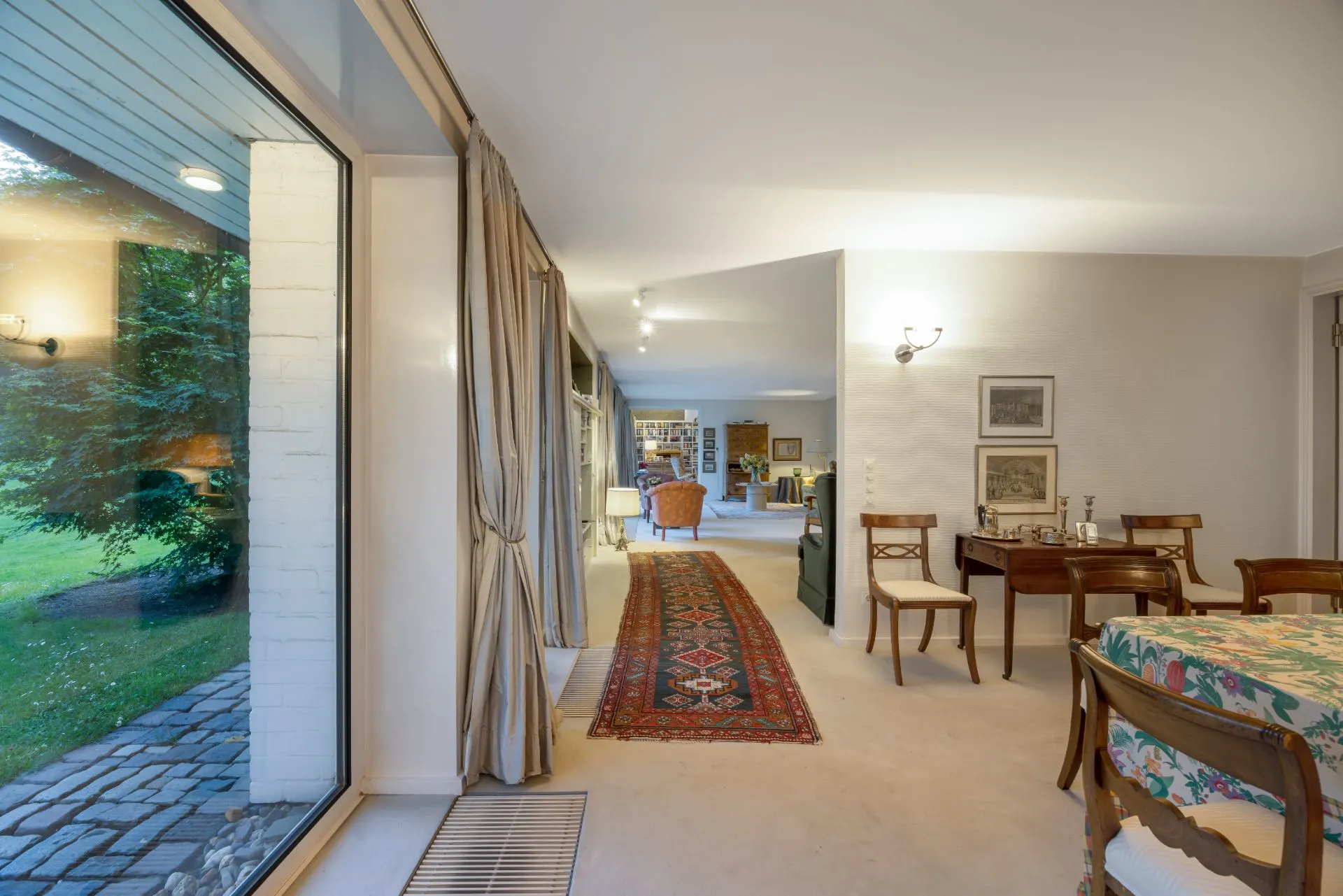 Wohnzimmer mit großem Fenster, Teppichläufer, Essbereich und Sitzmöbeln, Blick in den Garten.