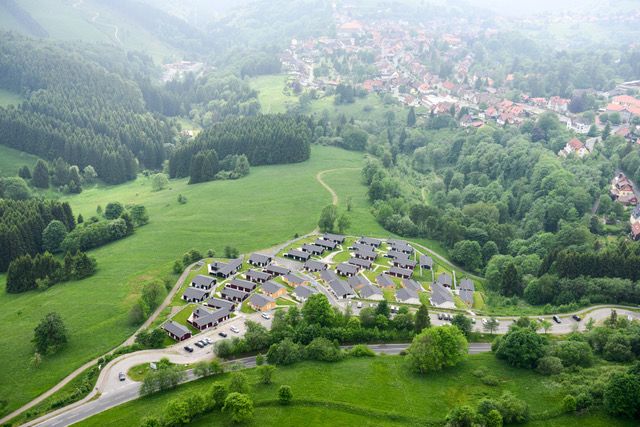 Luftaufnahme zeigt Wohnsiedlung mit Häusern im Grünen umgeben von Wäldern und Wiesen.