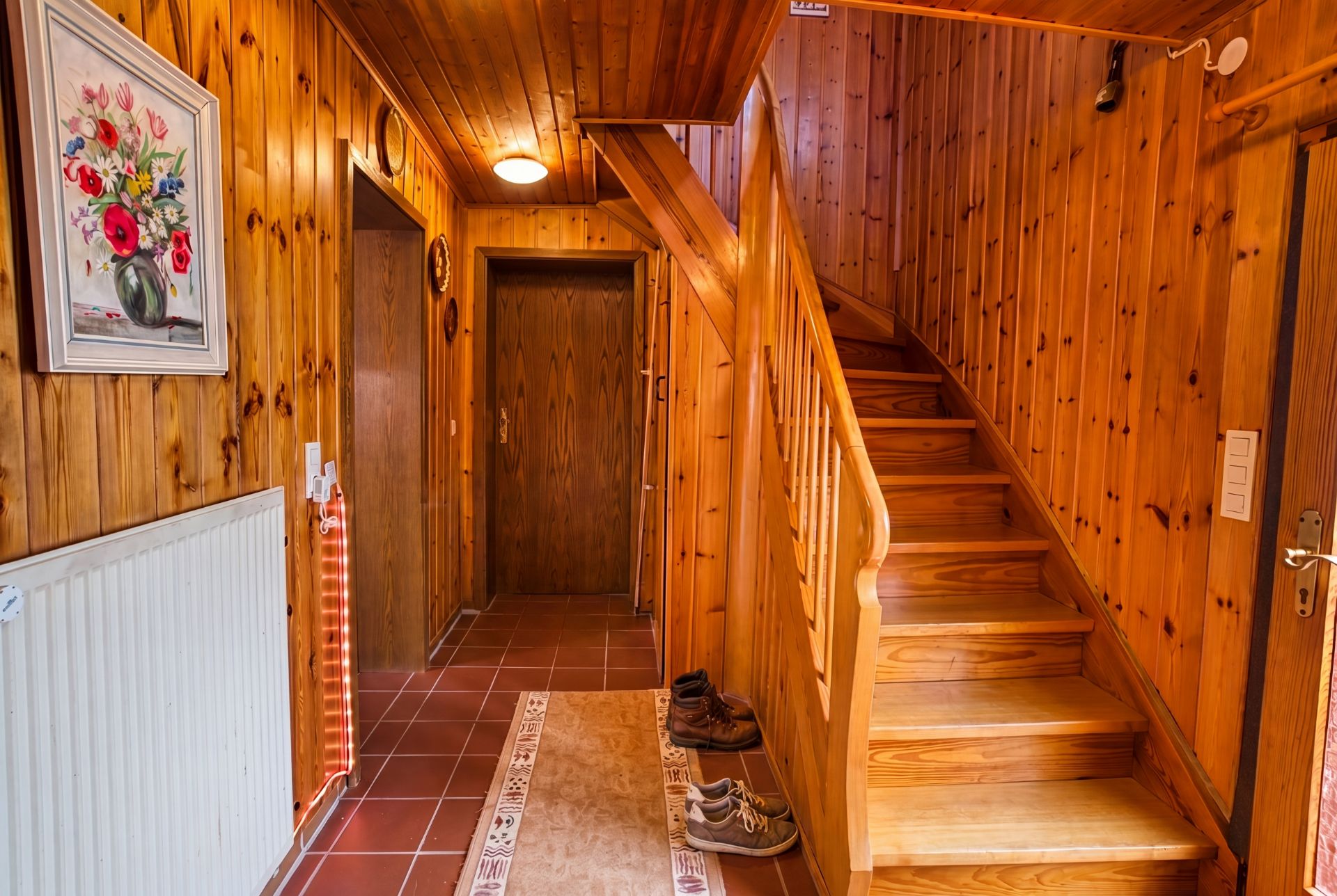 Flur mit Holzvertäfelung, Treppe, Schuhen auf dem Boden und Blumenbild an der Wand.