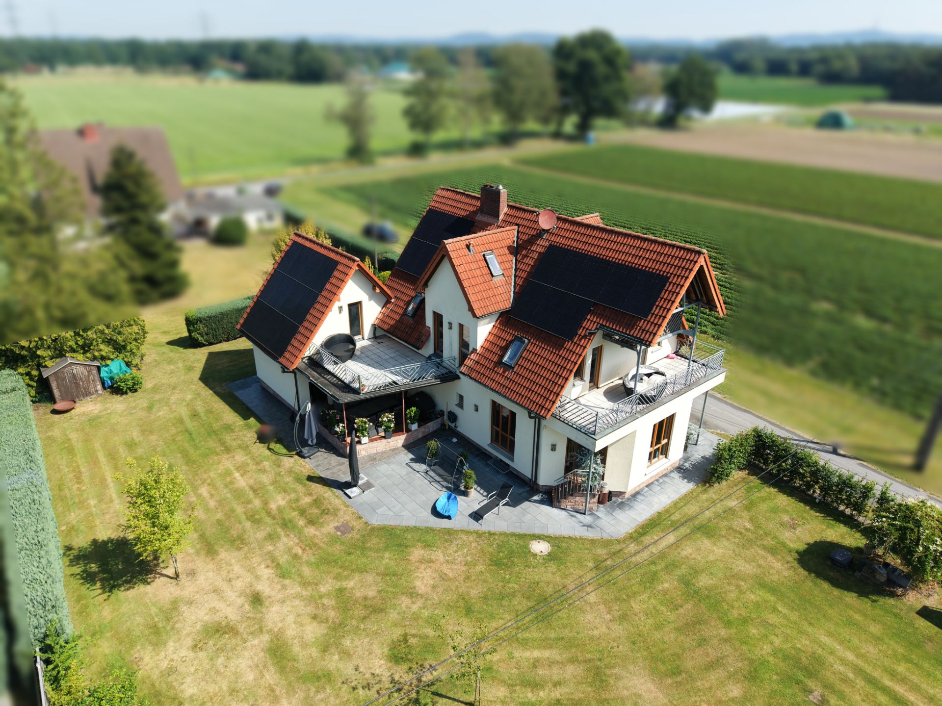 Luftaufnahme eines Einfamilienhauses mit roten Dachziegeln und Solarpanels im großen Garten.