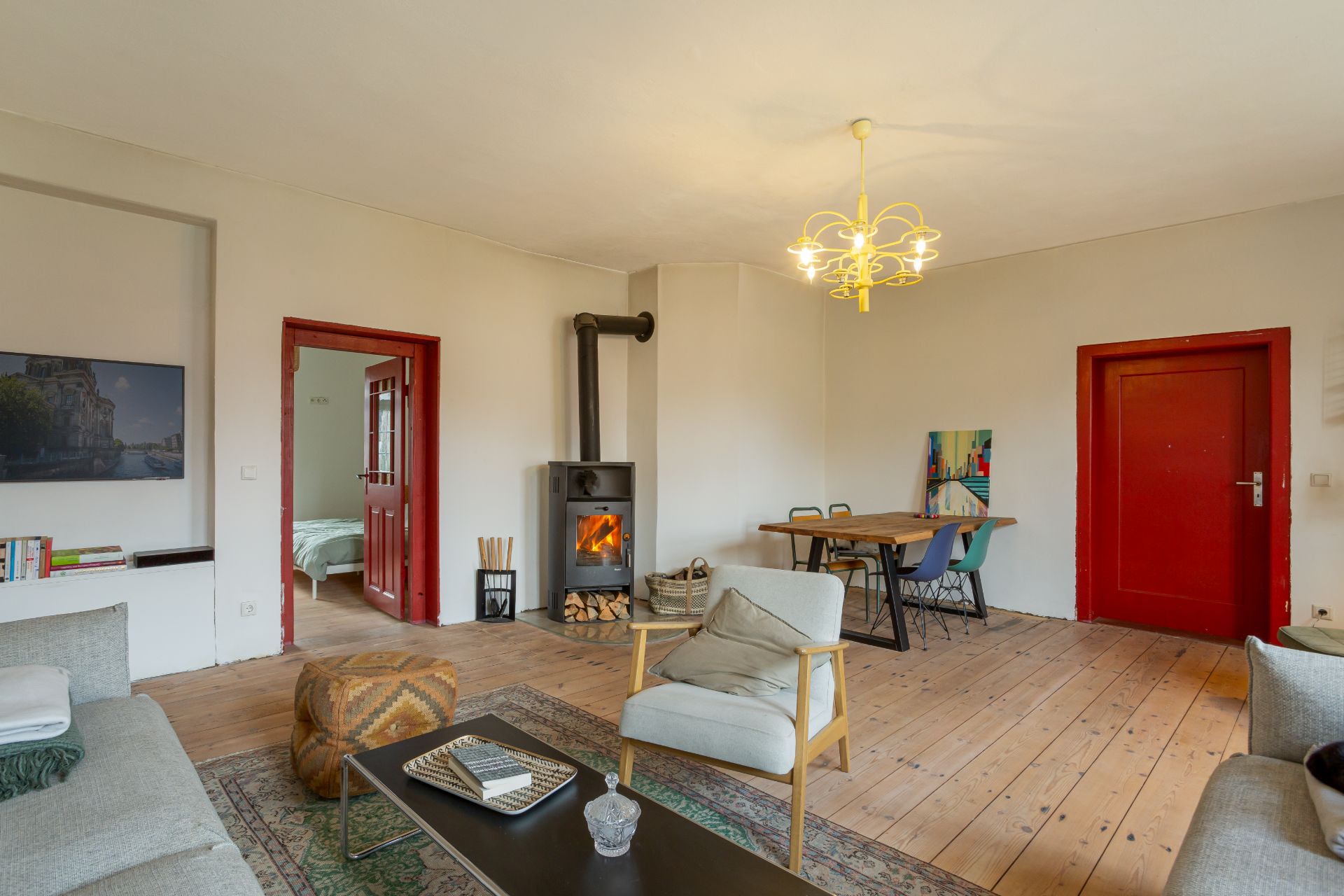 Helles Wohnzimmer mit Holzofen, Sitzbereich, Esstisch und roter Tür.