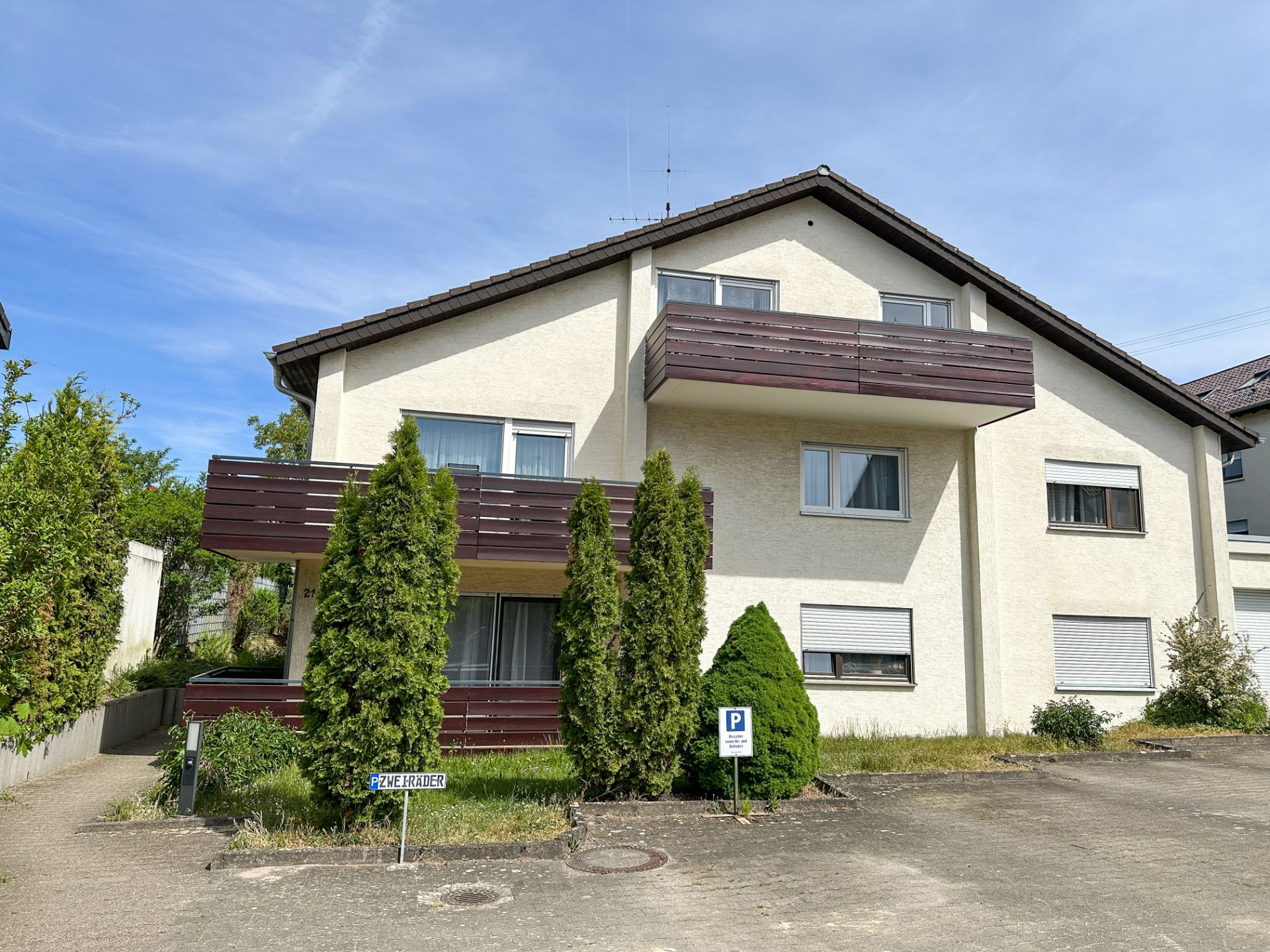 Zweistöckiges Wohnhaus mit Balkonen, Vorgarten und mehreren Parkplätzen vor dem Gebäude.