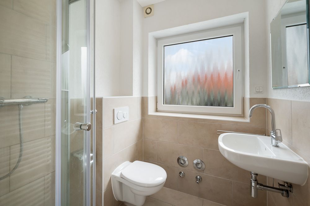 Modernes Badezimmer mit Dusche, wandhängender Toilette, Fenster und Waschbecken.