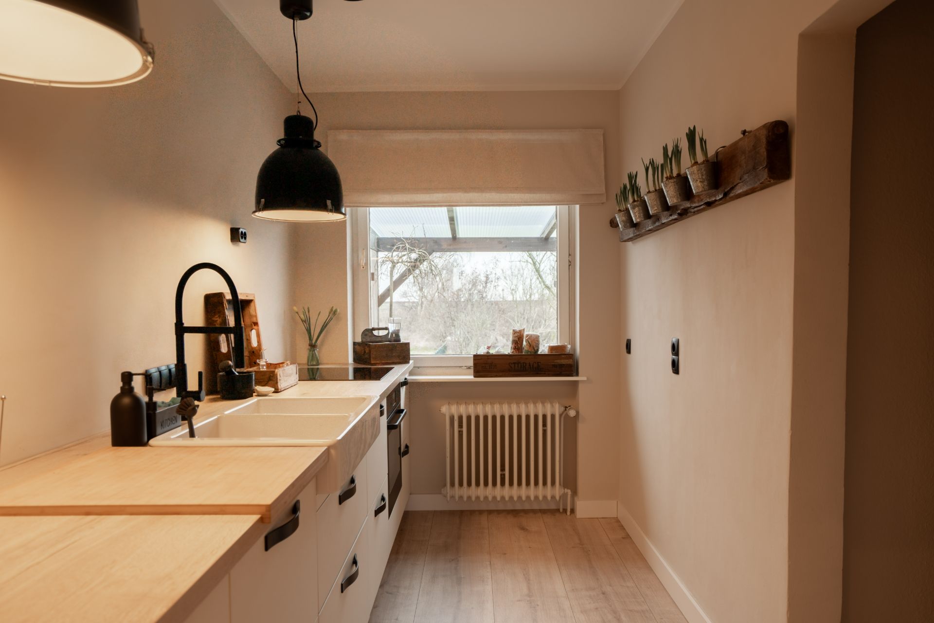Helle Küche mit Holzarbeitsplatte, Spüle, Hängelampe und Fenster mit Blick nach draußen.