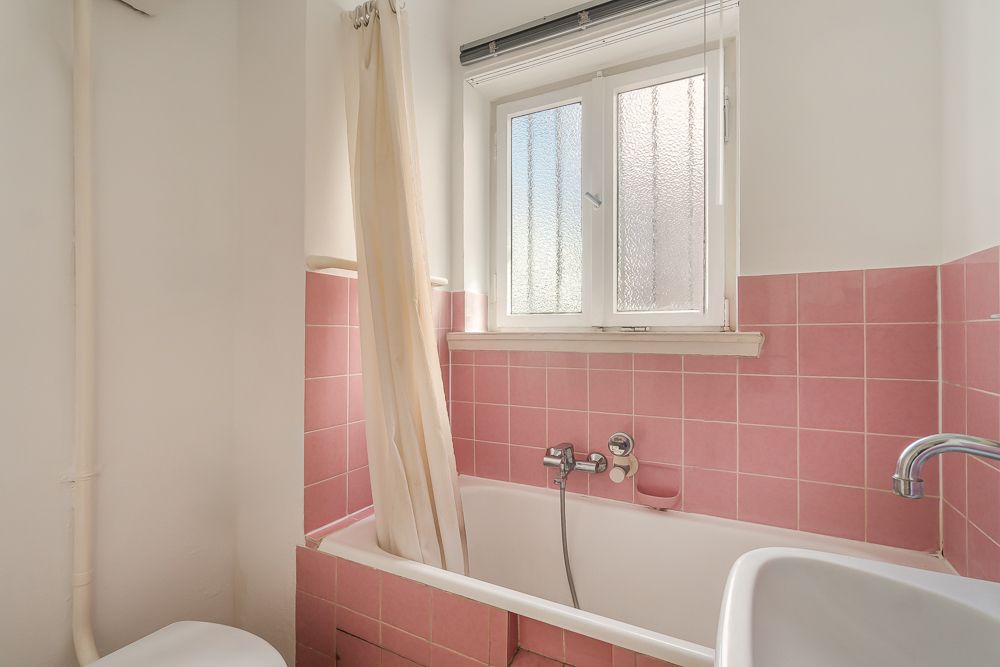 Bad mit rosa Fliesen, Badewanne, Duschvorhang und Fenster.