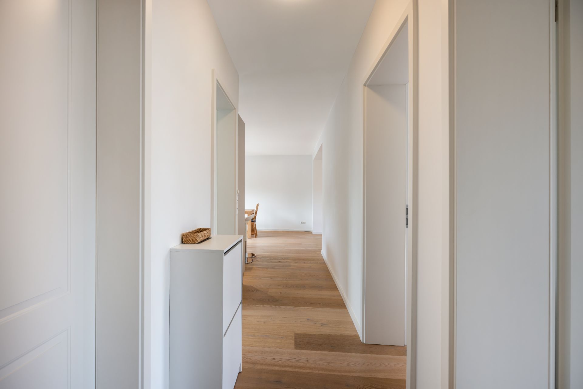 Heller Flur mit Holzboden, weißen Wänden und einer Kommode, Türen führen in weitere Räume.