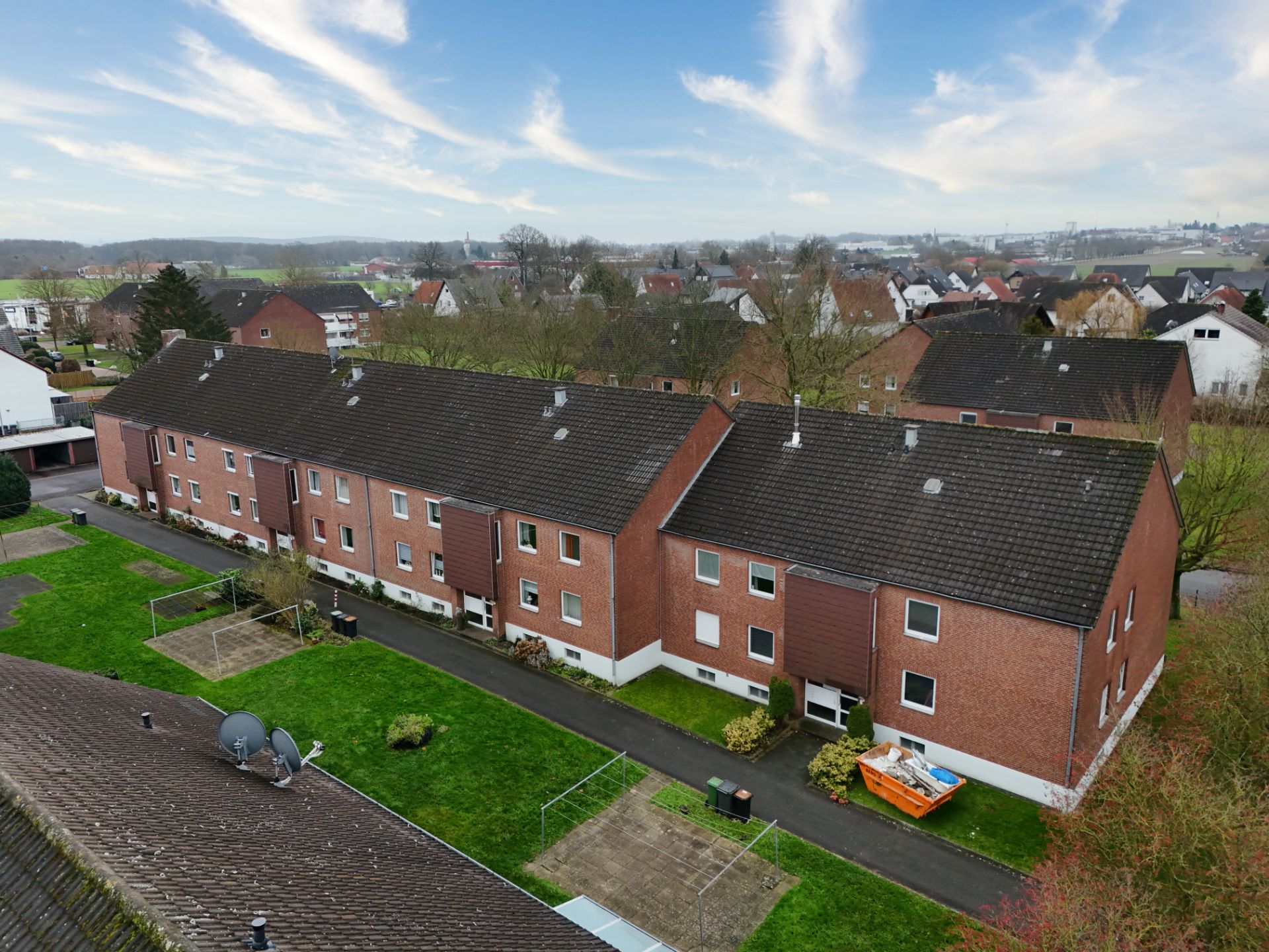 Mehrfamilienhaus aus rotem Klinker mit gepflegtem Rasen und Wegen, daneben einige Bäume.