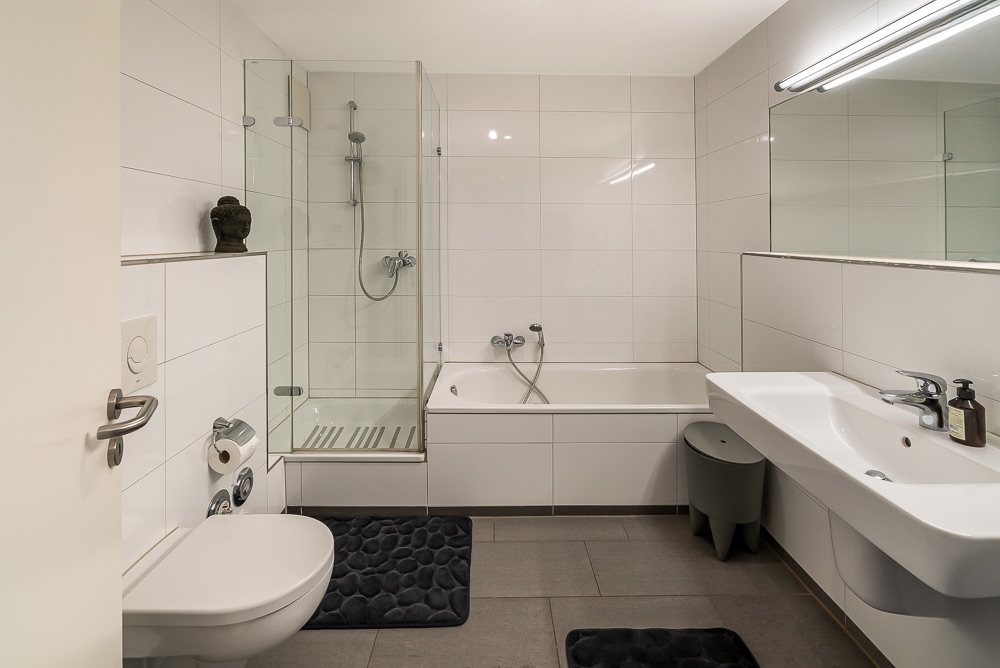 Modernes Badezimmer mit Toilette, Dusche, Badewanne, Waschbecken und großem Spiegel.