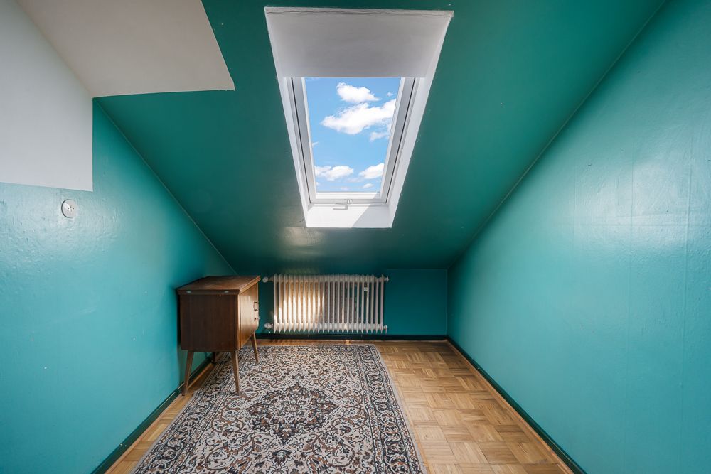 Kleines Zimmer mit schrägen, türkisfarbenen Wänden, Dachfenster und Teppichboden.