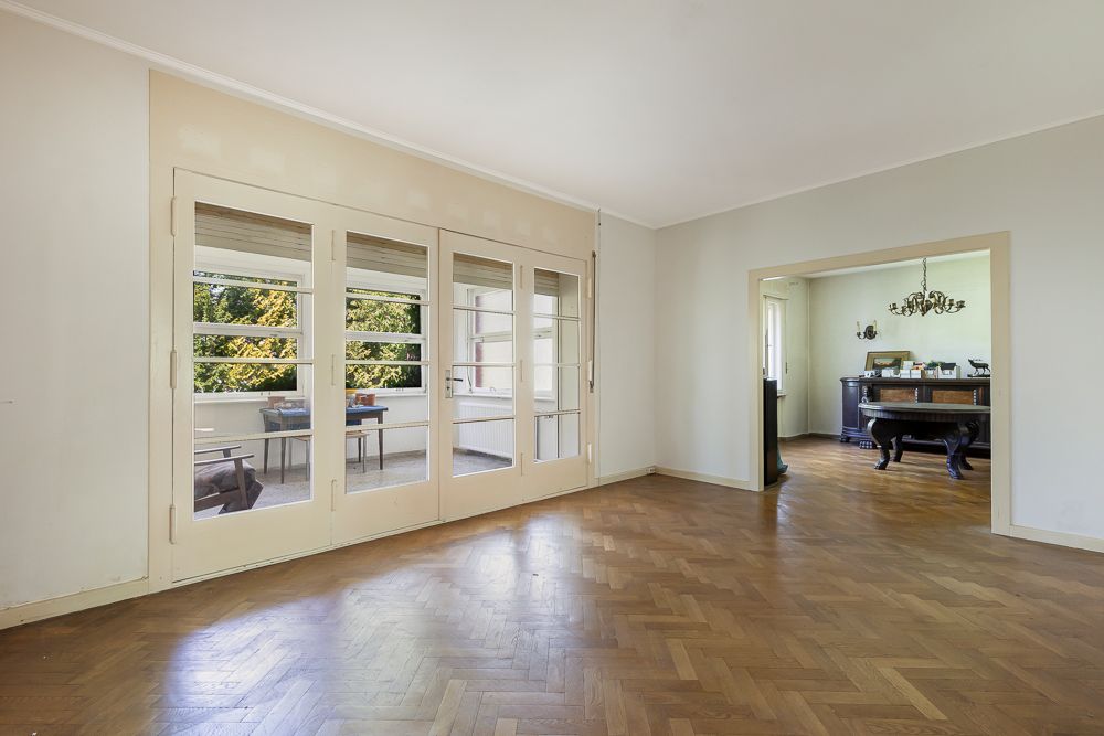 Helles Wohnzimmer mit Parkettboden, Glastüren und Blick auf einen angrenzenden Raum mit Esstisch.