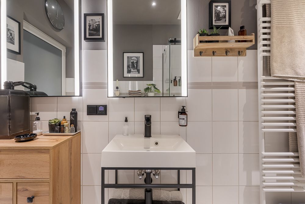 Modernes Badezimmer mit beleuchtetem Spiegel, Waschbecken, Handtuchheizkörper und Holzschrank.