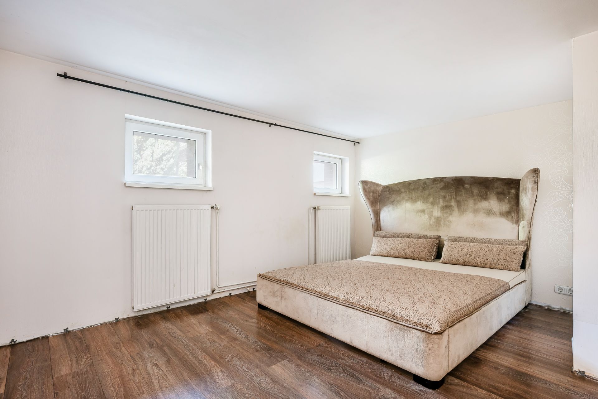 Schlafzimmer mit großem Bett, zwei Fenstern und Holzfußboden.