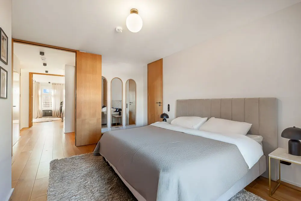 Helles Schlafzimmer mit großem Bett, Nachttischen und Spiegeln an der Wand.