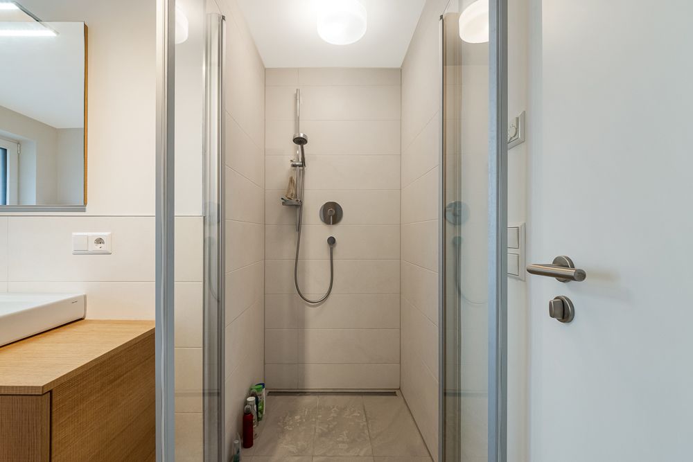Moderne, begehbare Dusche mit Glaswänden und Handbrause in einem hellen Badezimmer.