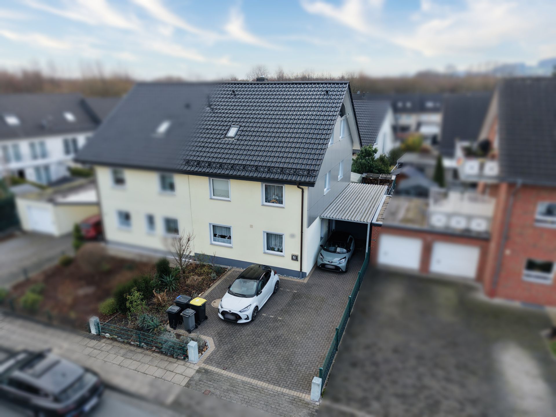 Doppelhaushälfte mit zwei Autos in Einfahrt und gepflegtem Vorgarten.