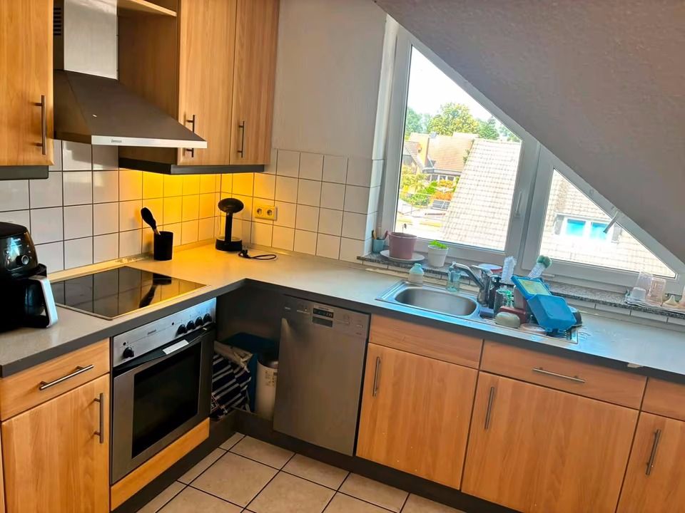 Moderne Einbauküche mit Holzmöbeln, Herd, Spülmaschine, Spüle und großem Fenster unter Dachschräge.
