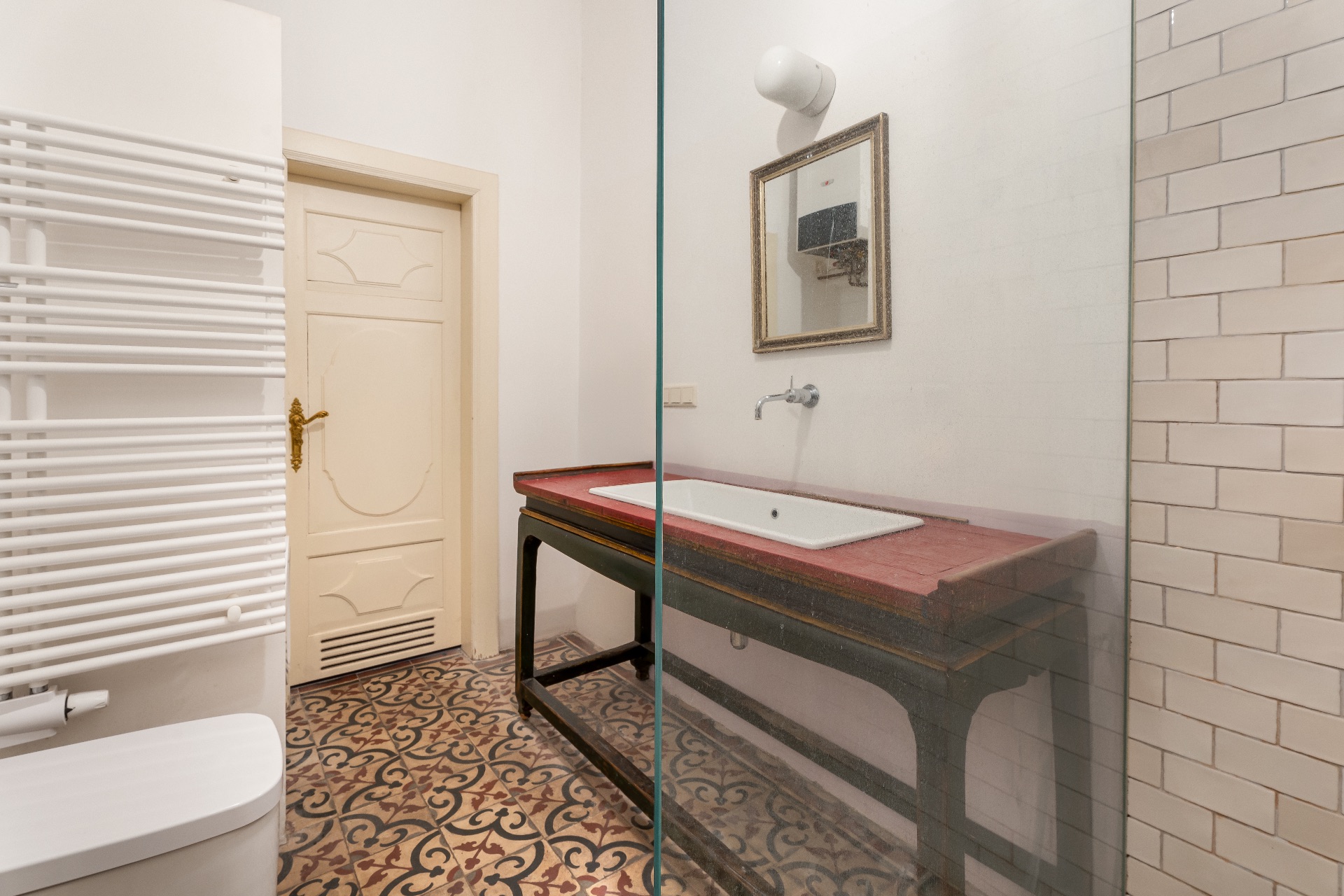 Modernes Badezimmer mit gemustertem Fliesenboden, Waschbecken, Spiegel und weißer Tür.