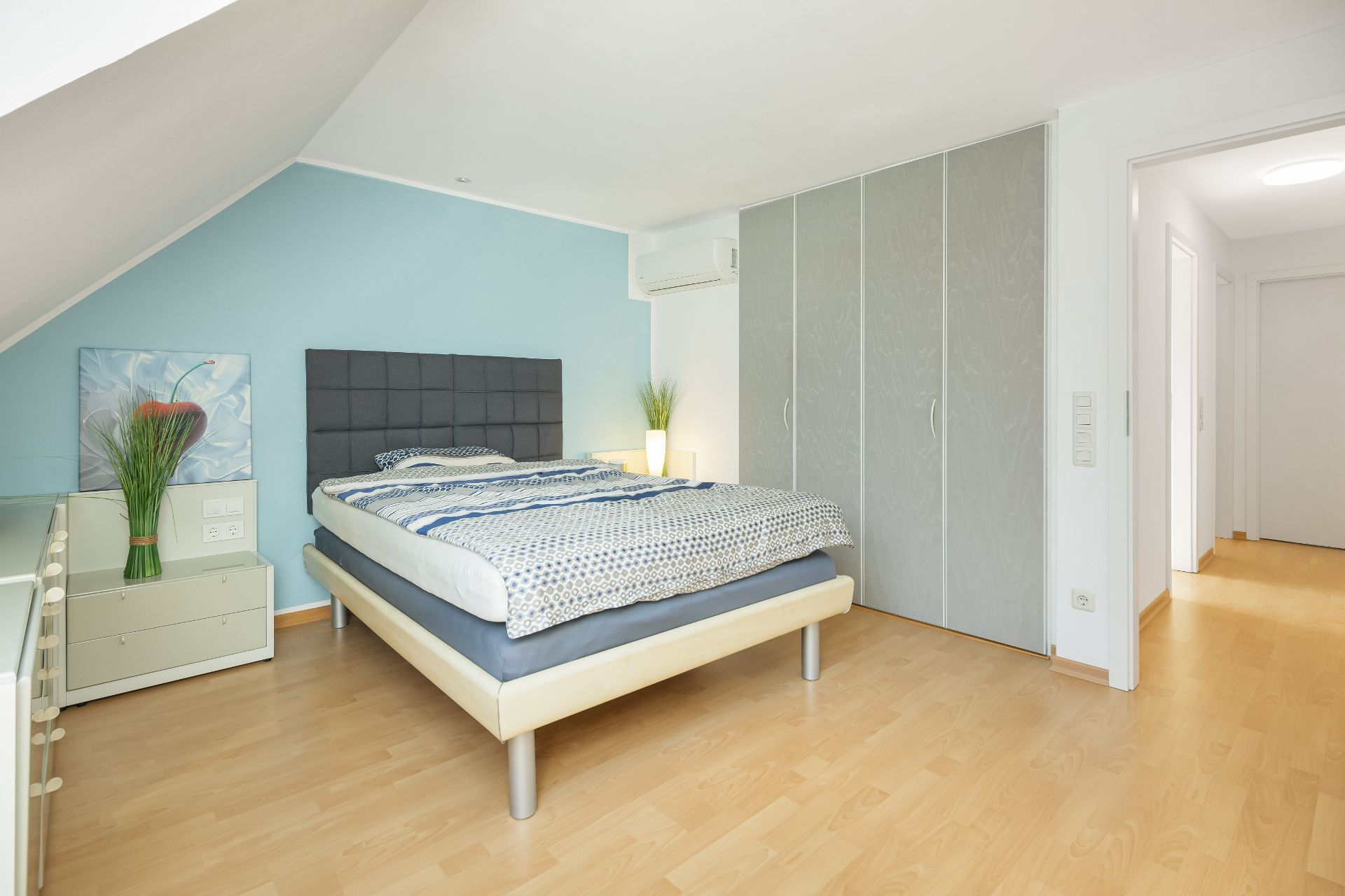 Helles Schlafzimmer mit Doppelbett, großem Kleiderschrank und Nachttisch auf Holzfußboden.