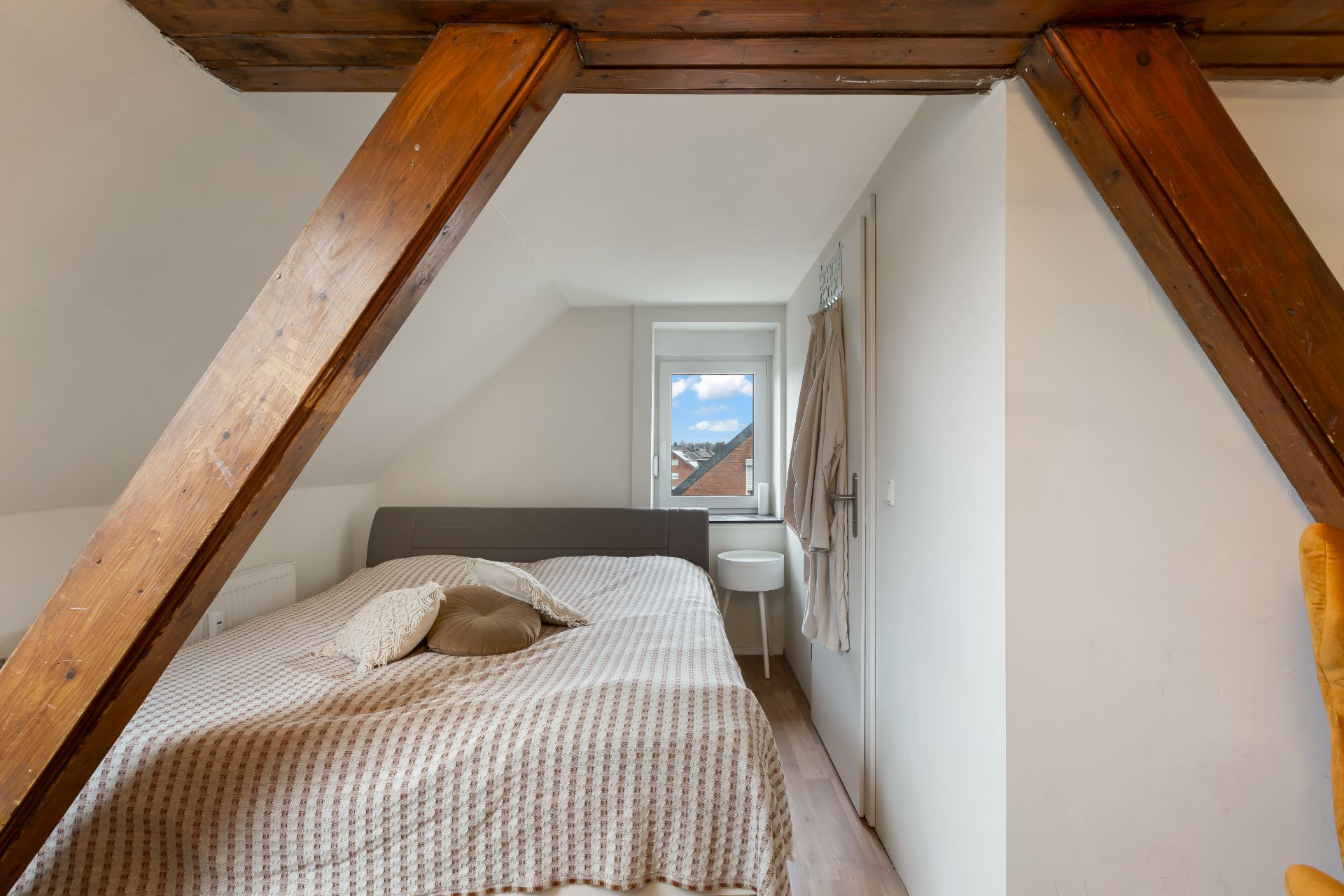 Schlafzimmer mit Holzbalken, Doppelbett und Fenster an der Stirnwand.