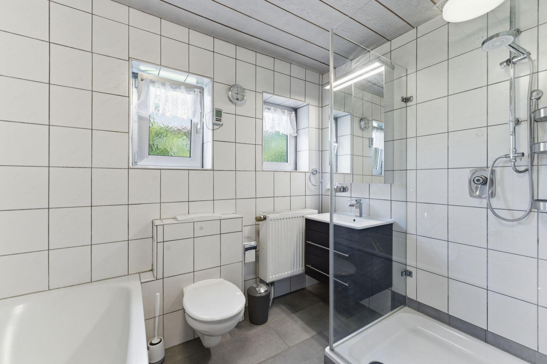 Modernes Badezimmer mit Dusche, WC, Waschbecken, Badewanne und zwei kleinen Fenstern.