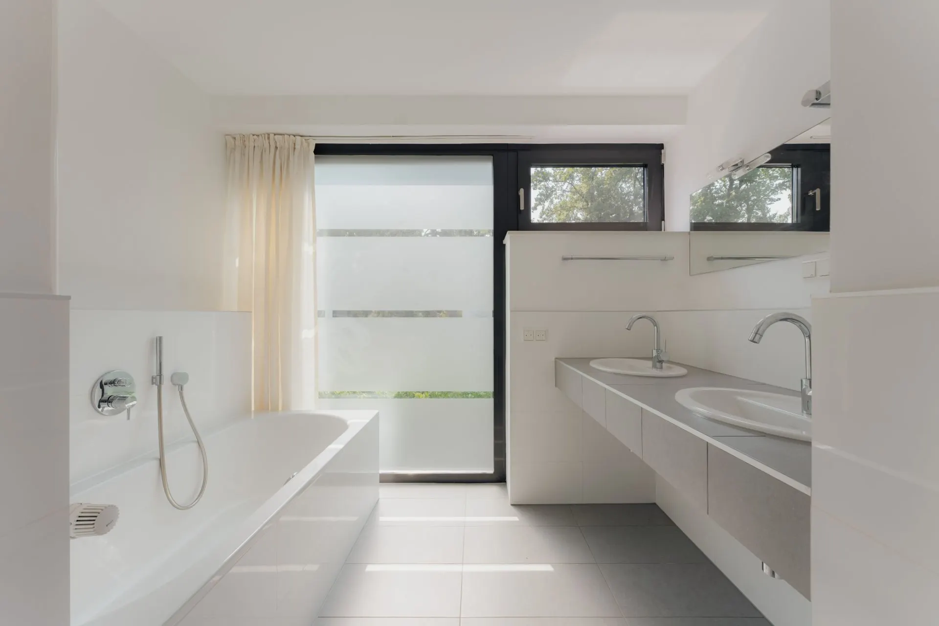 Modernes Badezimmer mit Badewanne, zwei Waschbecken und großem Fenster mit Milchglas.