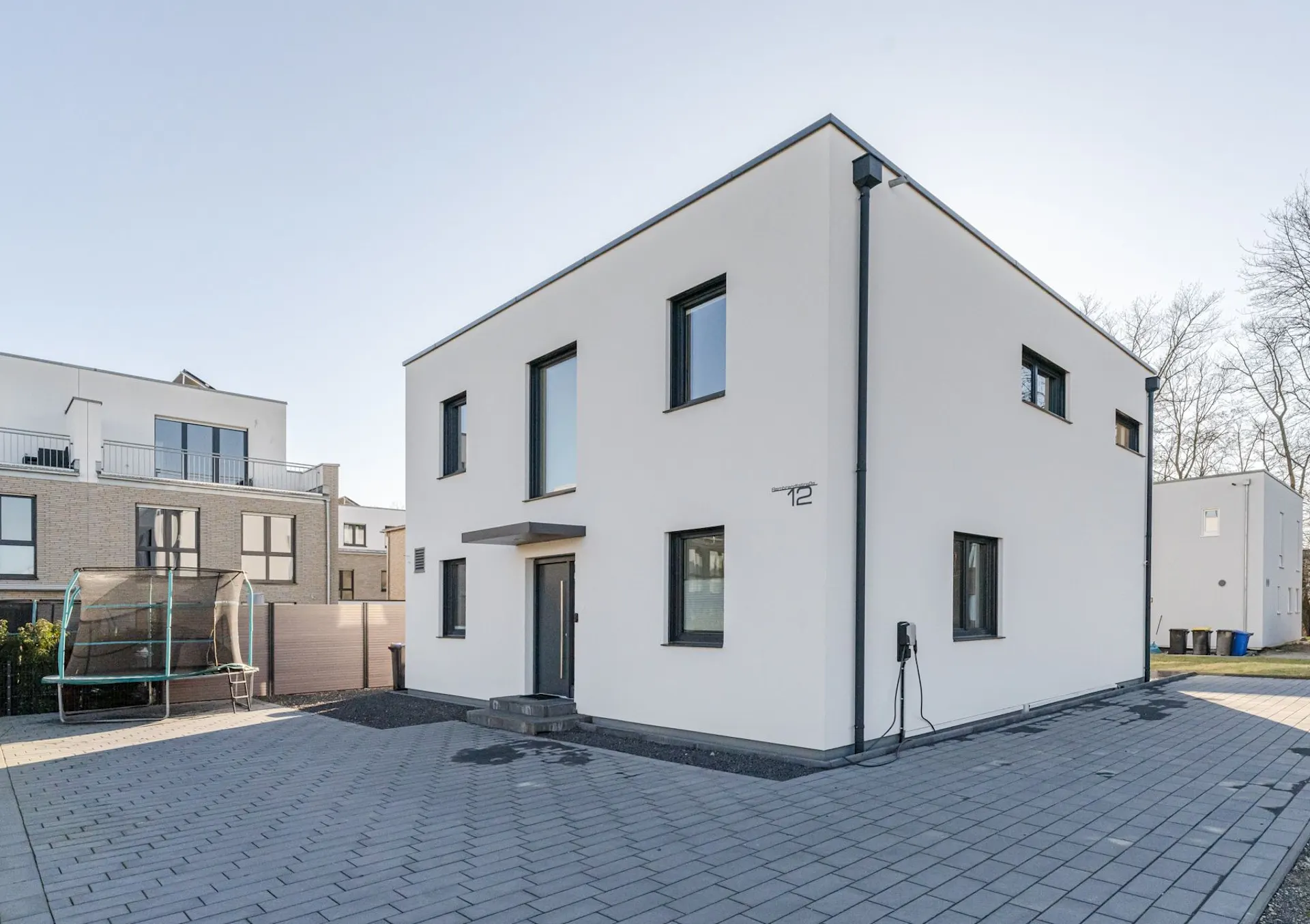 Modernes, weißes Einfamilienhaus mit flachem Dach und gepflastertem Vorhof.