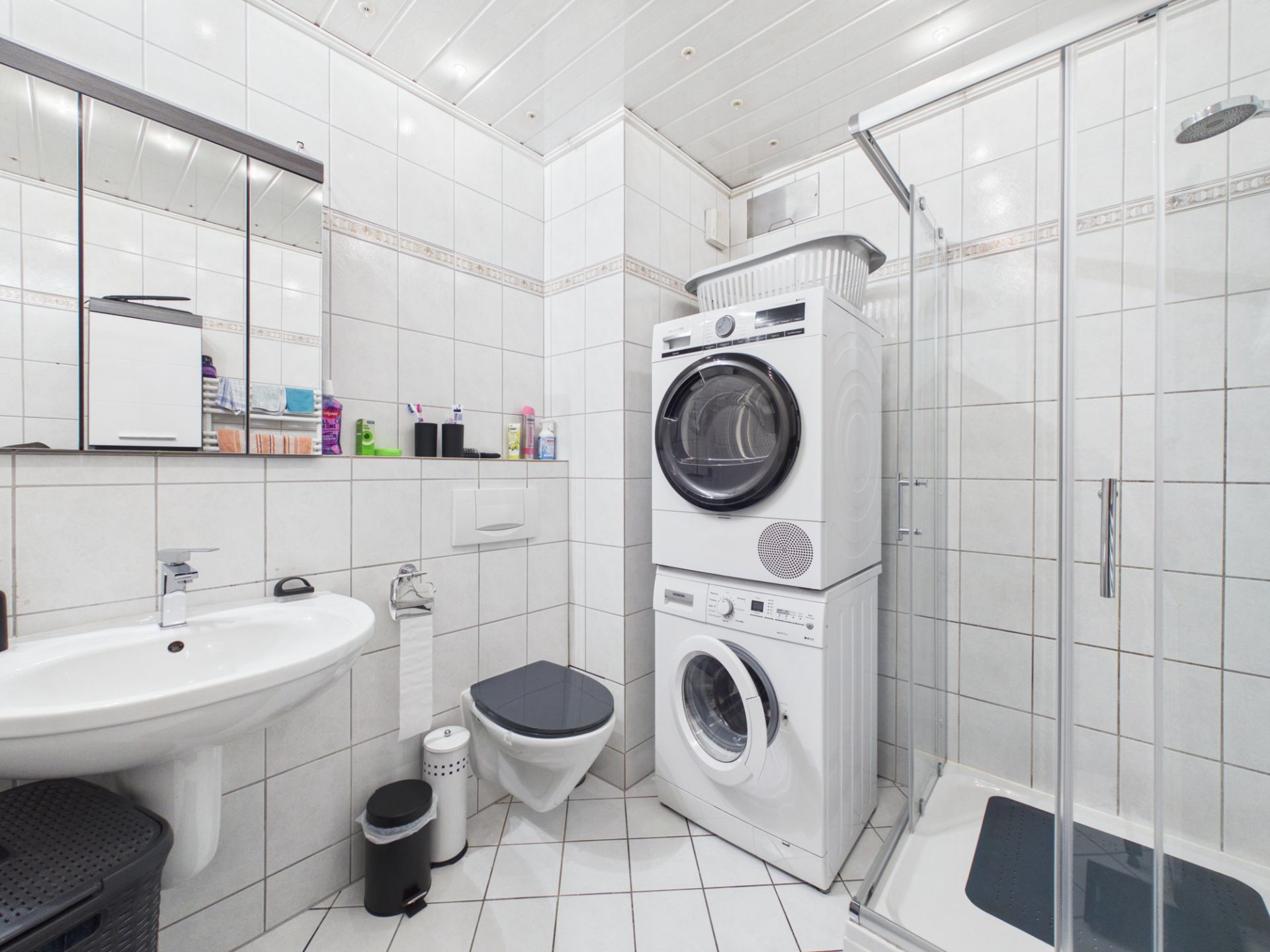 Modernes Badezimmer mit Waschbecken, WC, Dusche und gestapelter Waschmaschine und Trockner.