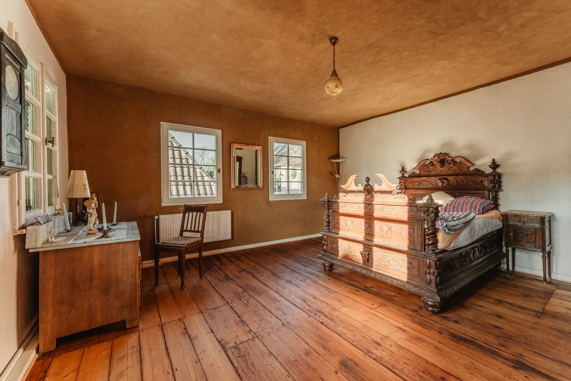 Schlafzimmer mit einem großen, geschnitzten Holzbett, Holzboden, Schreibtisch und Stuhl.