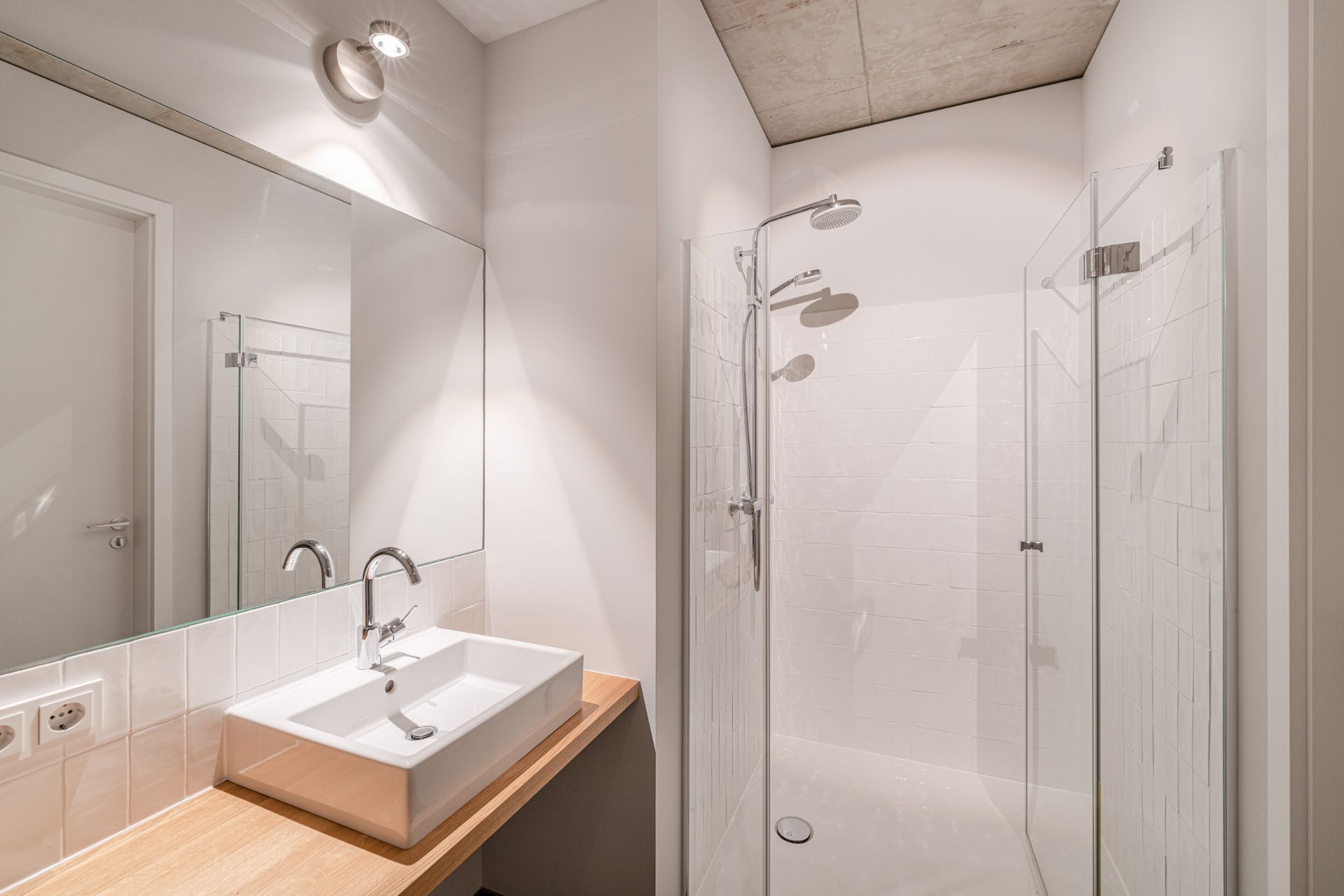 Modernes Badezimmer mit großem Spiegel, Waschbecken und ebenerdiger Dusche mit Glaswand.