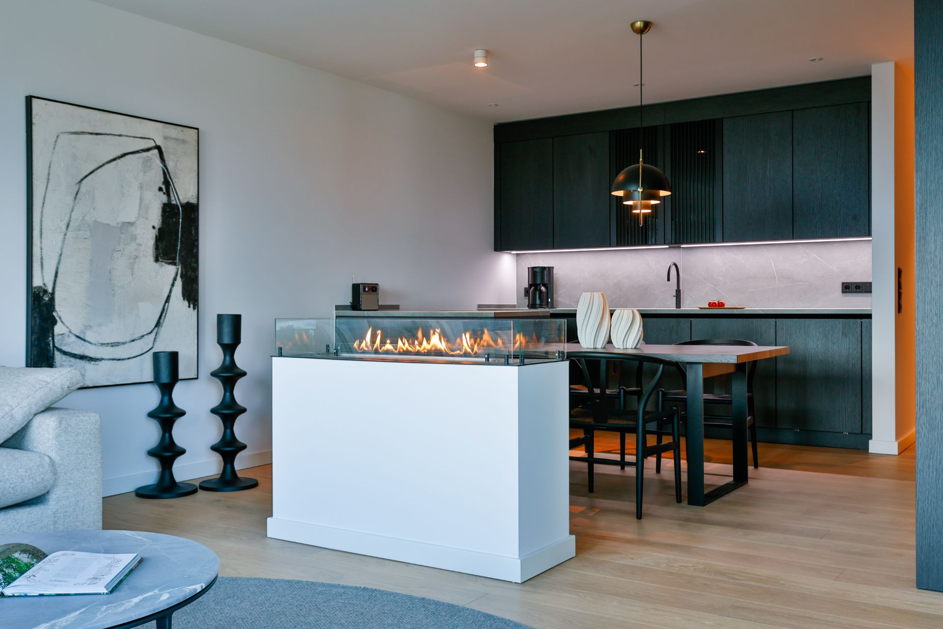 Moderne Wohnküche mit Kamin, Esstisch, schwarzen Schränken und abstraktem Bild an der Wand.