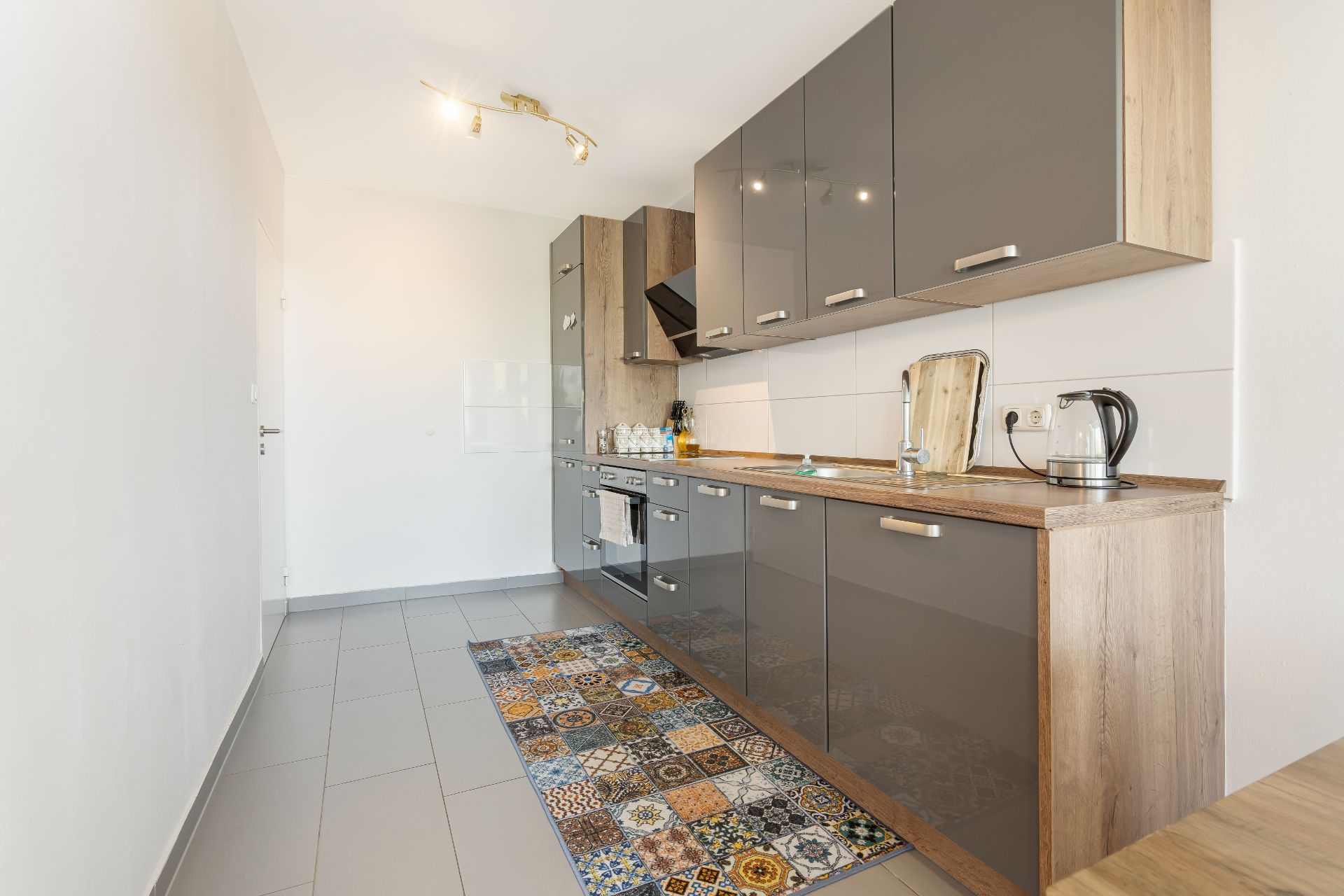 Moderne Einbauküche mit grauen Hochglanzfronten und gemustertem Teppichläufer.