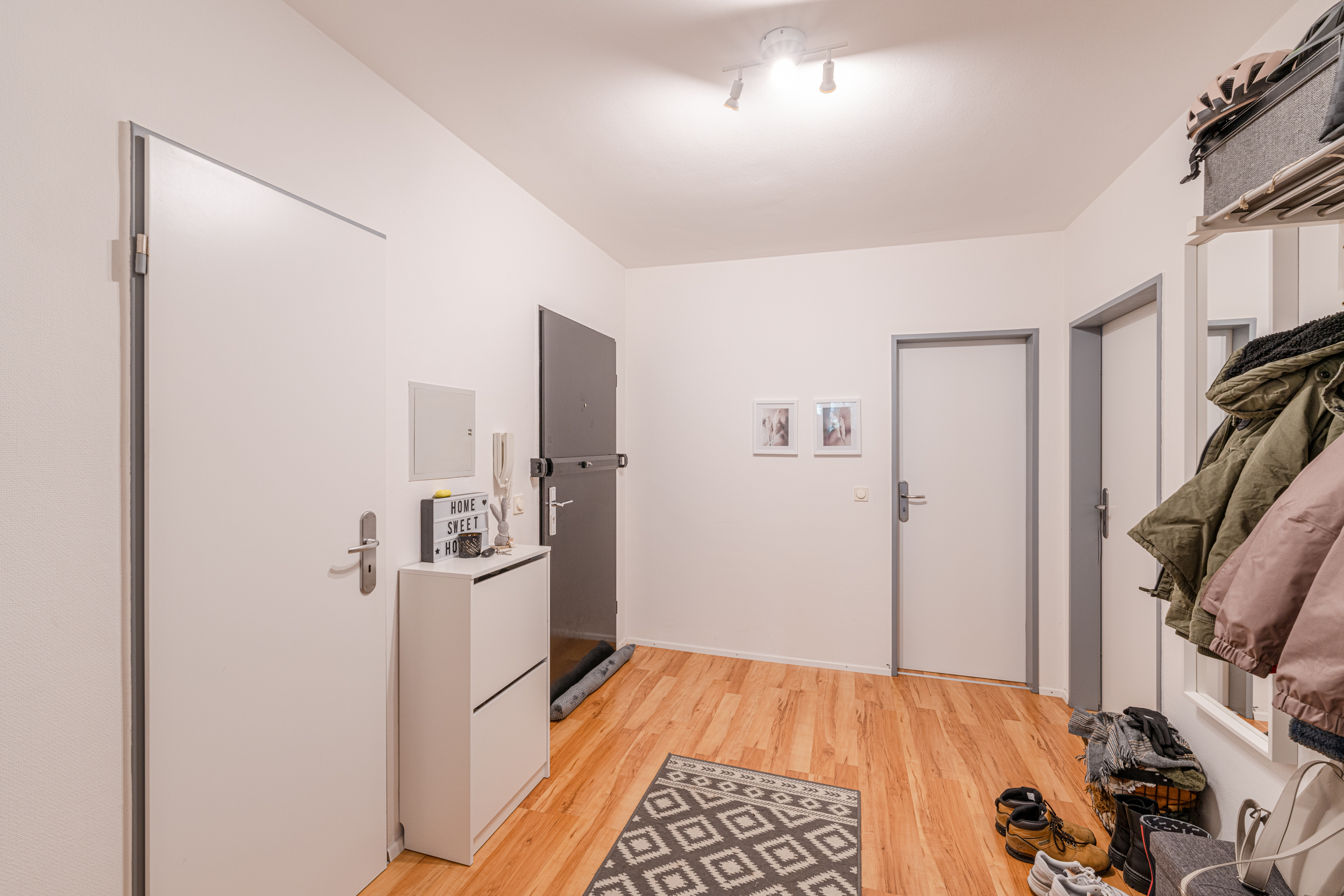 Heller Flur mit Holzboden, Garderobe, Schuhregal und mehreren weißen Türen.