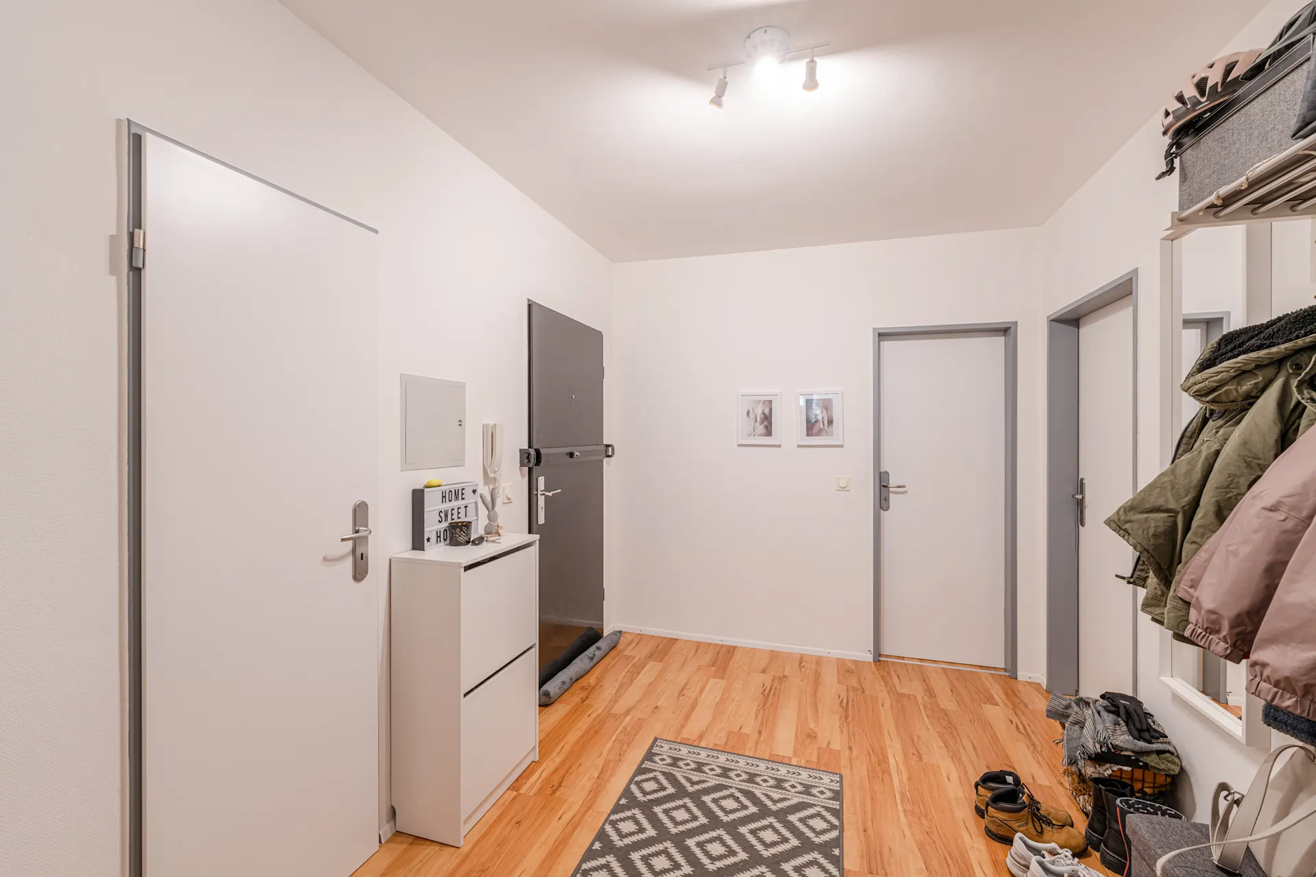 Heller Flur mit Holzboden, Garderobe, Schuhregal und mehreren weißen Türen.