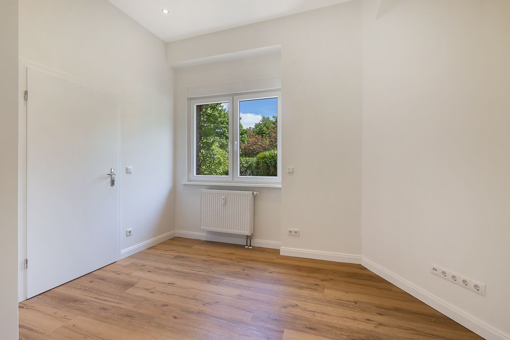 Leerer Raum mit Holzfußboden, weißer Wand, Fenster und Heizkörper.